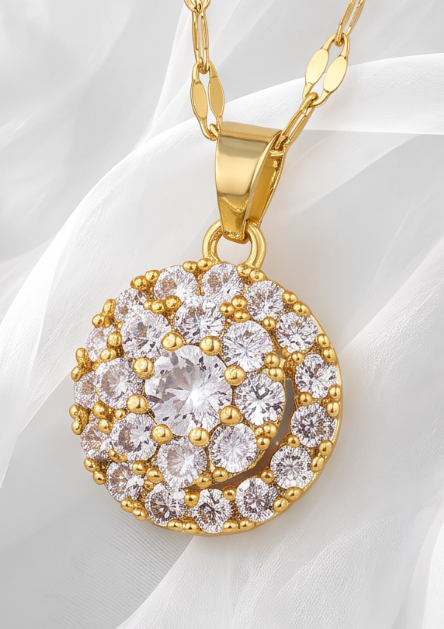 A gold pendant necklace featuring a circular cluster of clear cubic zirconia stones, displayed on a soft white fabric background.