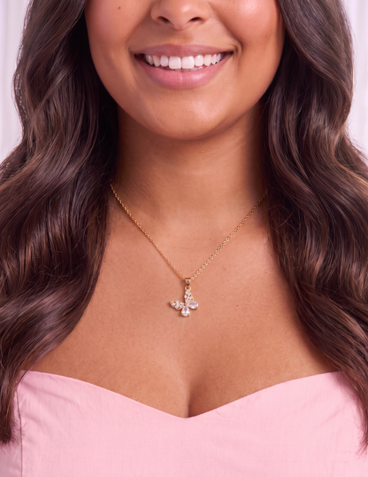 A close-up lifestyle shot of a woman wearing a delicate gold chain necklace with a small bird pendant adorned with clear crystals, paired with a light pink top.