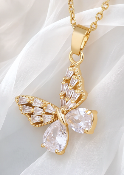 Gold butterfly pendant necklace with clear baguette and teardrop crystals, displayed on a soft white fabric background.