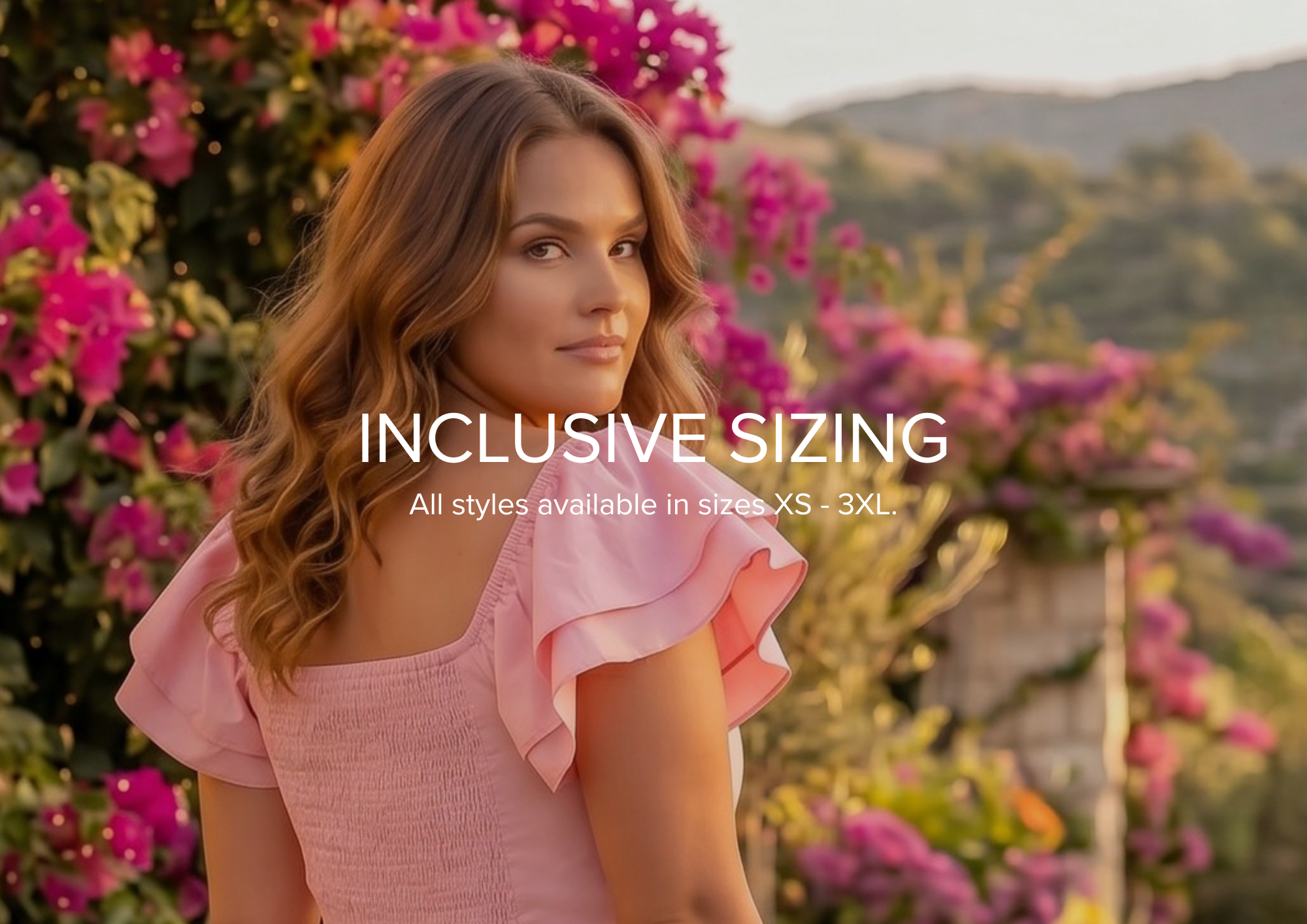 A woman wearing a light pink ruffled top stands outdoors among pink flowers, with overlaid text reading 'INCLUSIVE SIZING' and smaller text below.