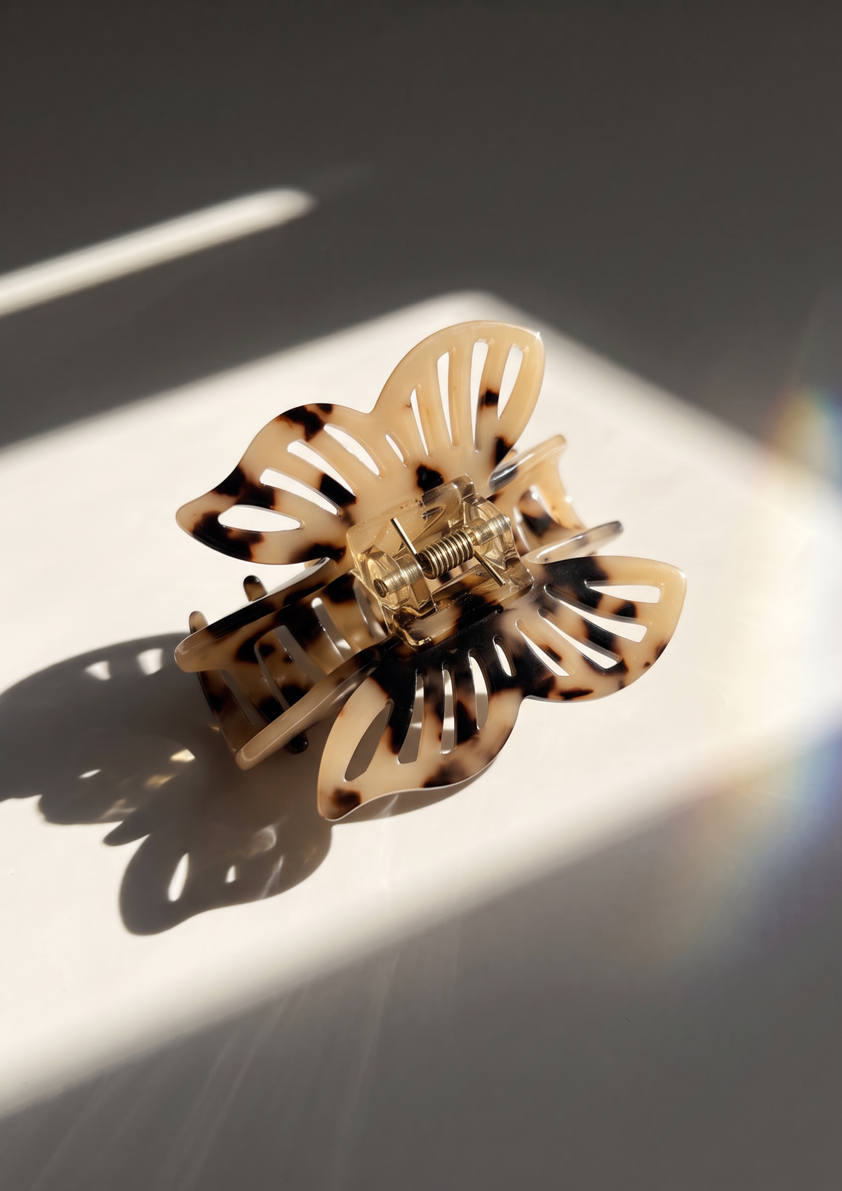 A tortoiseshell butterfly-shaped hair claw clip resting on a white surface with dramatic diagonal sunlight and shadows.