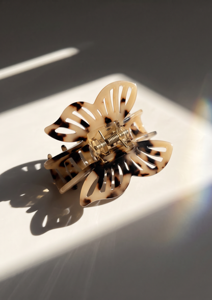 A tortoiseshell butterfly-shaped hair claw clip resting on a white surface with dramatic diagonal sunlight and shadows.