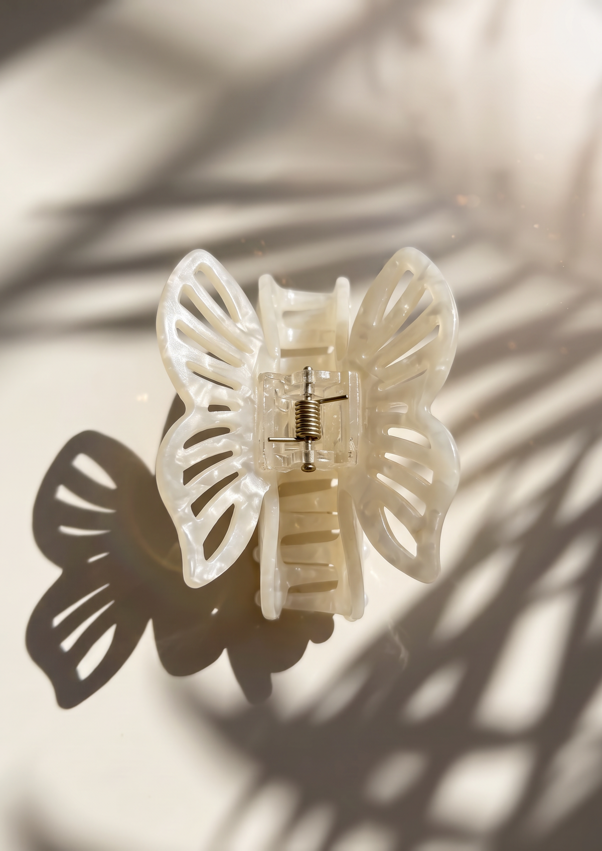 A translucent white butterfly-shaped hair claw clip with a butterfly shadow cast on a light beige background.