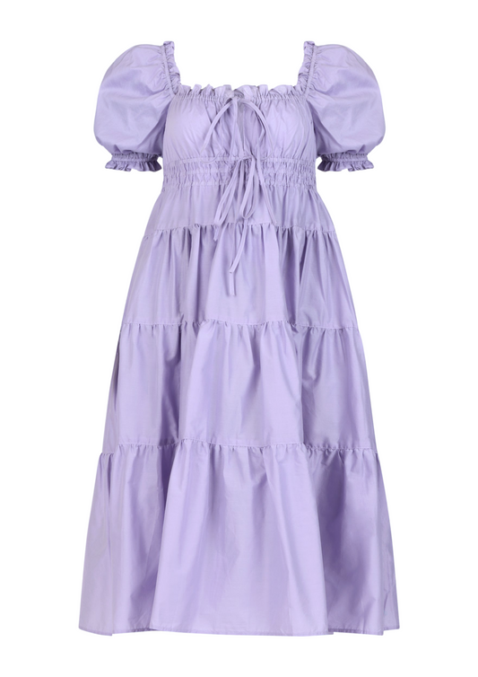 Elegant lilac midi dress with puff sleeves – the Penelope Dress by Eravela, crafted from organic cotton with a tiered skirt, adjustable bow ties, and a flattering cinched waist. Perfect for weddings, brunch, garden parties, and summer occasions. A feminine and timeless flowy dress designed for effortless elegance and comfort.